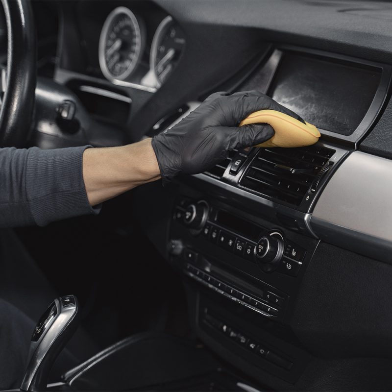 Man in a garage. Worker polish inside a car. Man in a black uniform.